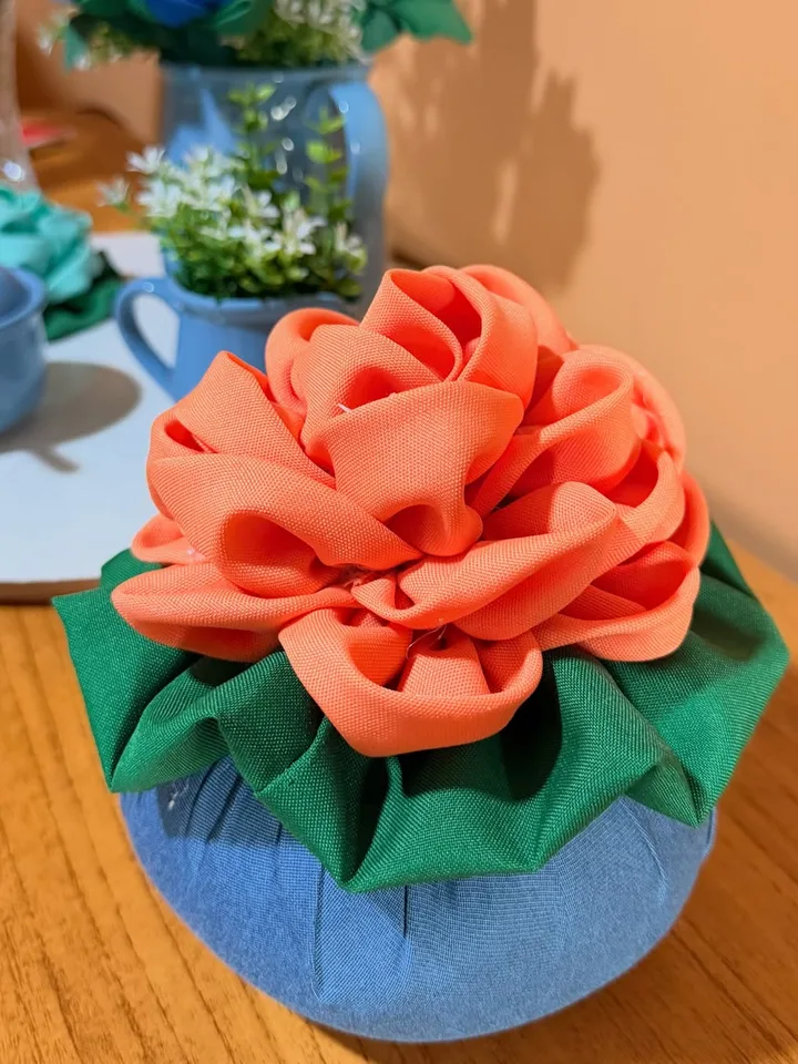 Close de flor de pano coral com folhas verdes sobre corpo azul de tecido