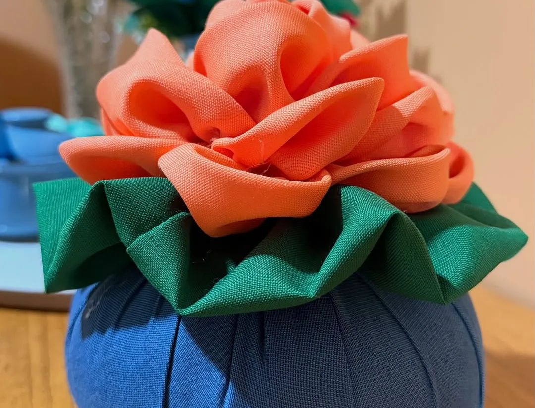 Peso de porta artesanal em uma mesa de madeira, com flores e objetos domésticos ao fundo